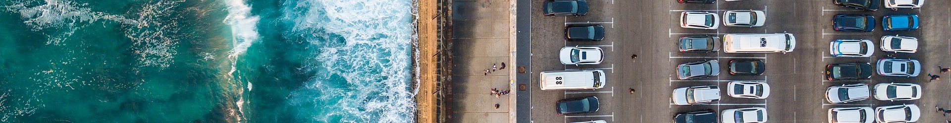 Aerial view of ocean waves crashing beside a busy coastal car park